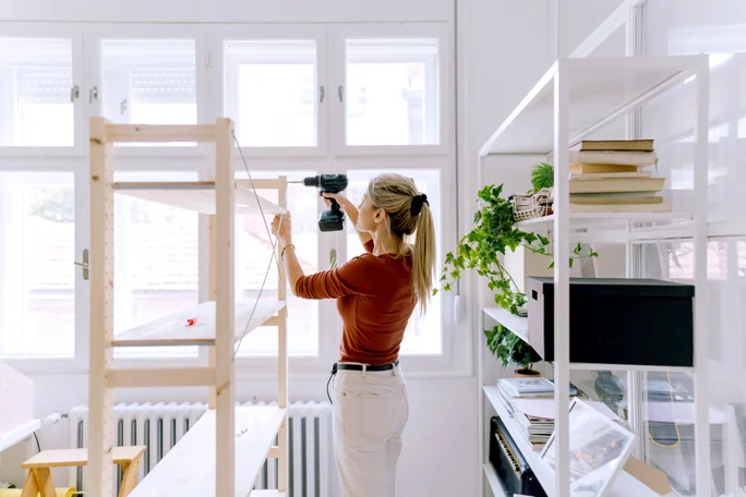 Photo of a young woman moving into a new apartment, assembling new furniture on the floor.